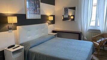Camera d'albergo con un letto, comodini, una sedia, una finestra con tende e lampade a parete.
