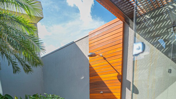 Una terraza de madera con un ventanal que da a un espacio cubierto, rodeada de abundante vegetación.
