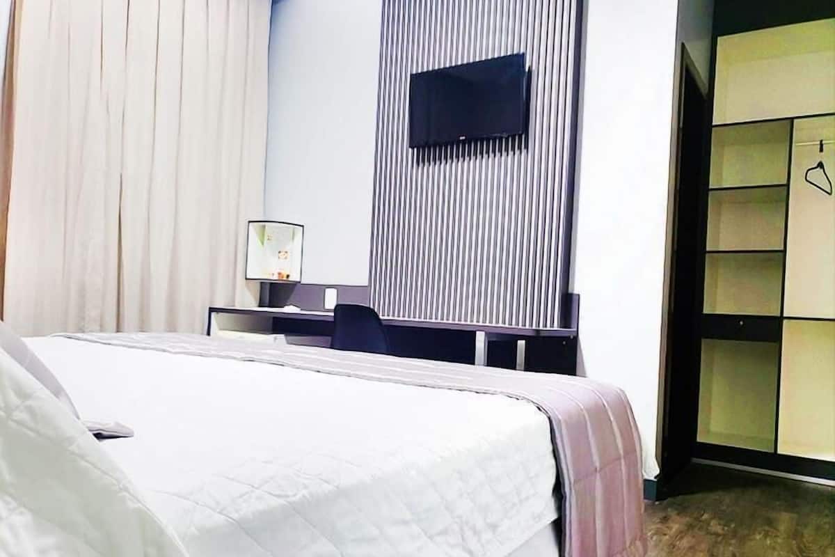 Une chambre d’hôtel comprenant un lit, un bureau avec une chaise, un téléviseur fixé au mur et une armoire.