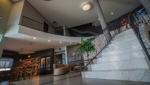 Un vestíbulo amplio con una escalera de mármol, zona de estar y una tienda a la vista.