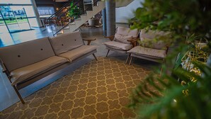 Un vestíbulo con un sofá, sillones, un tapete estampado, una escalera y plantas de interior.