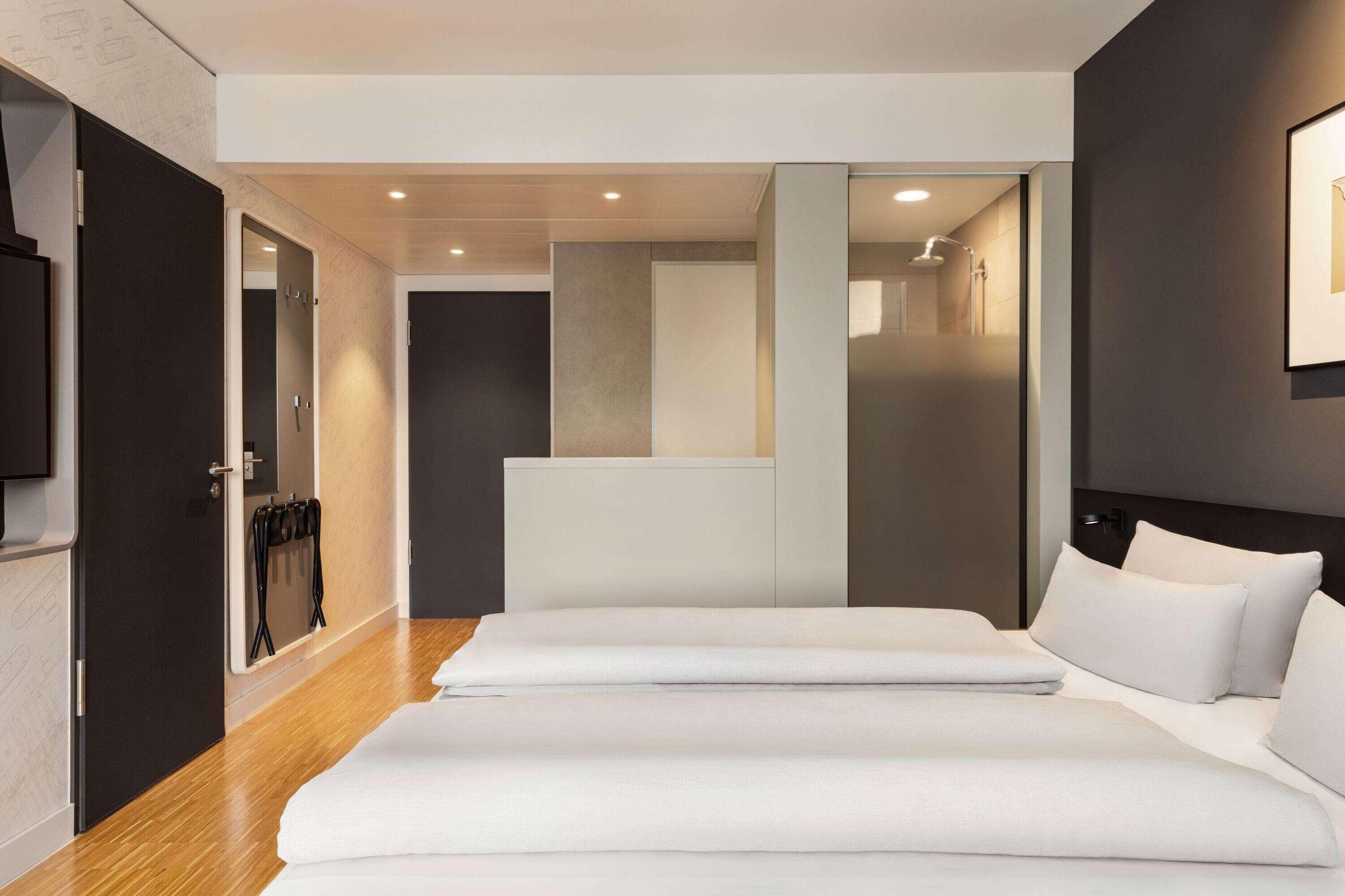 Ein modernes Hotelzimmer mit einem großen Bett, Holzboden und Blick auf den Gang.