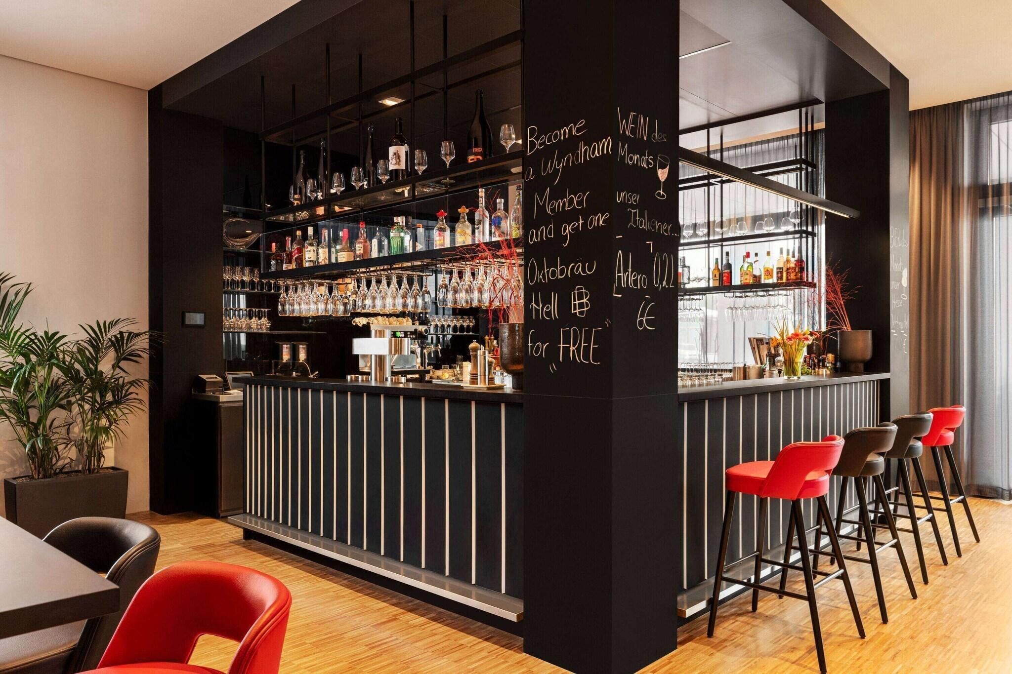 A bar area with shelves of bottles and glasses, a chalkboard with text, and red bar stools.