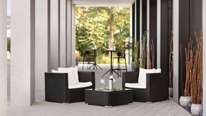 A covered outdoor seating area with wicker furniture and a glass table, surrounded by tall plants and a view of trees. - Ernst Leitz Hotel Wetzlar (Wetzlar)
