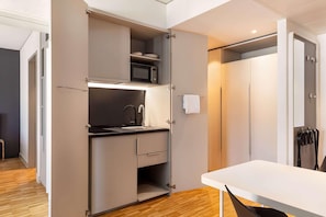 A compact kitchen with a microwave, sink, and cabinets, adjacent to a white table and a door with a towel rack. - Ernst Leitz Hotel Wetzlar (Wetzlar)