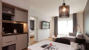 A modern hotel room with a kitchenette, a dining area, a TV, and a comfortable seating area with a sofa and a coffee machine. - Ernst Leitz Hotel Wetzlar (Wetzlar)