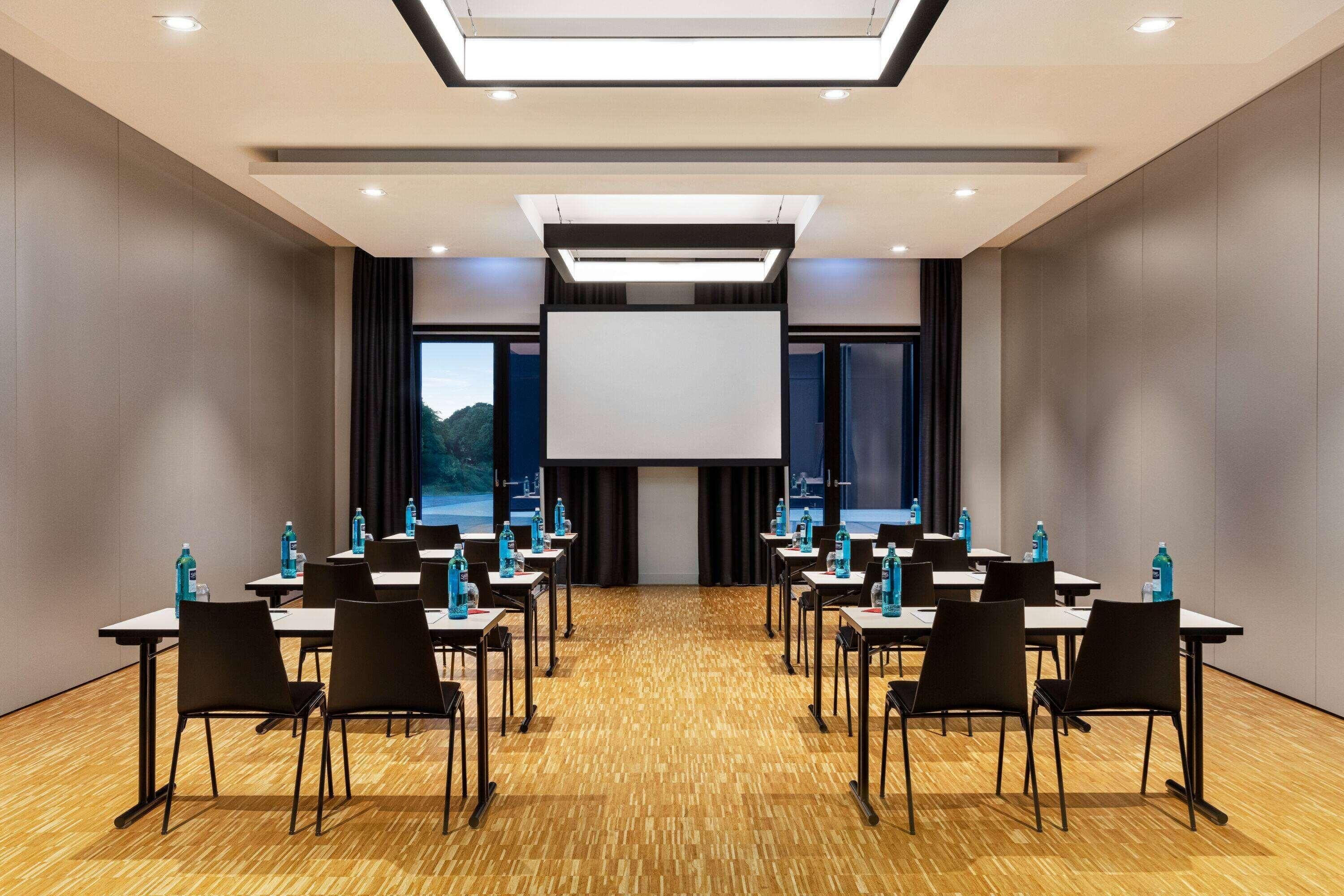 A conference room with a large screen, tables, chairs, and water bottles.
