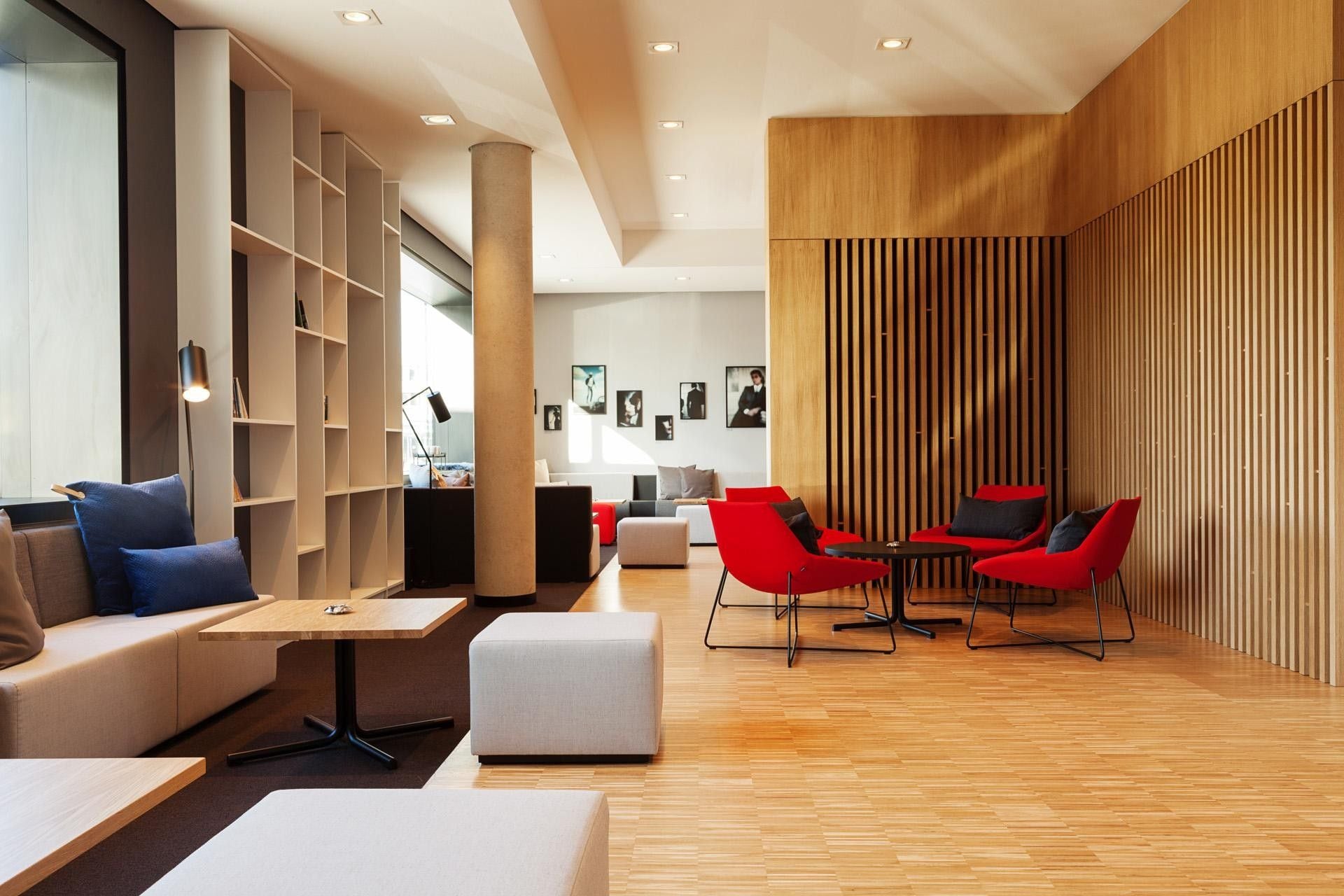Um interior moderno com piso de madeira, área de estar com cadeiras vermelhas, um sofá branco e uma estante de livros.