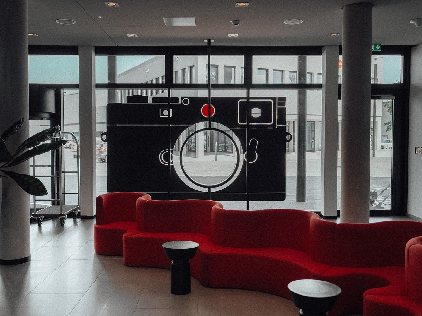 A modern lobby with red seating, a large window, and a unique wall art installation.