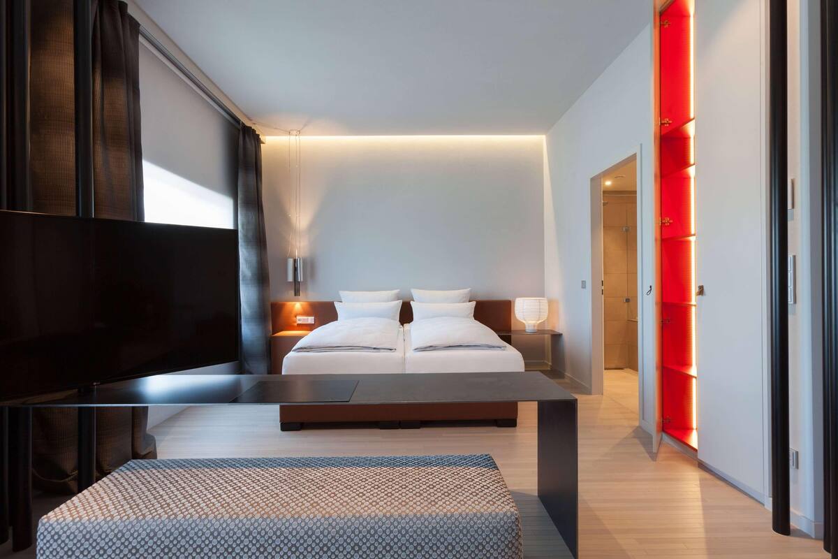 A modern bedroom with a large bed, bedside tables, a flat-screen TV, and a red-lit shelving unit.