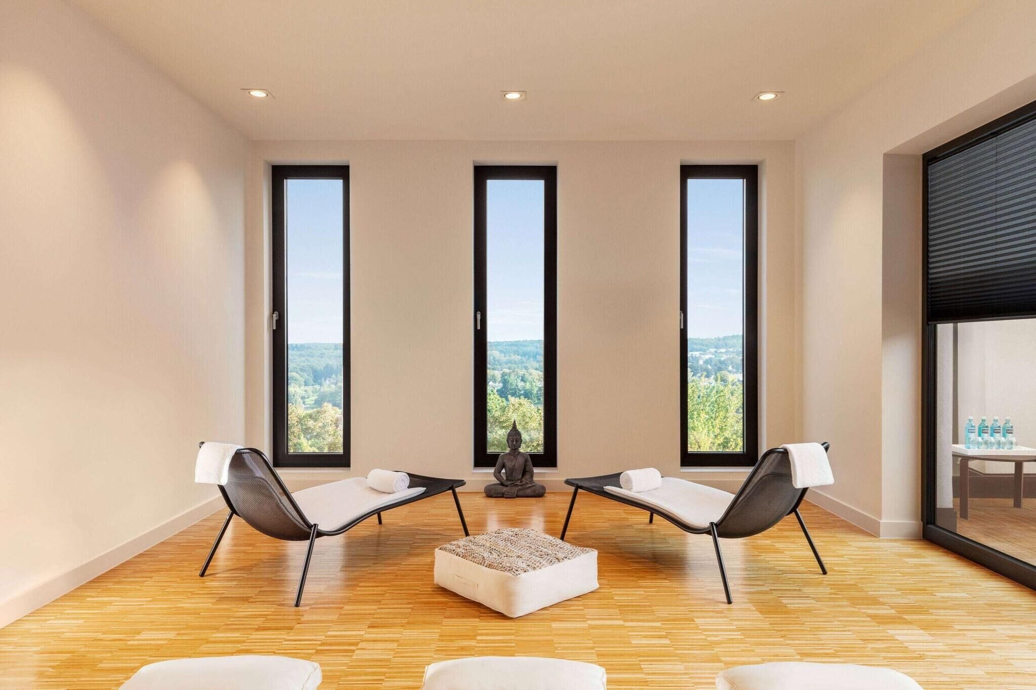 A modern room with three large windows, two lounge chairs, a meditation statue, and a small table with water bottles.