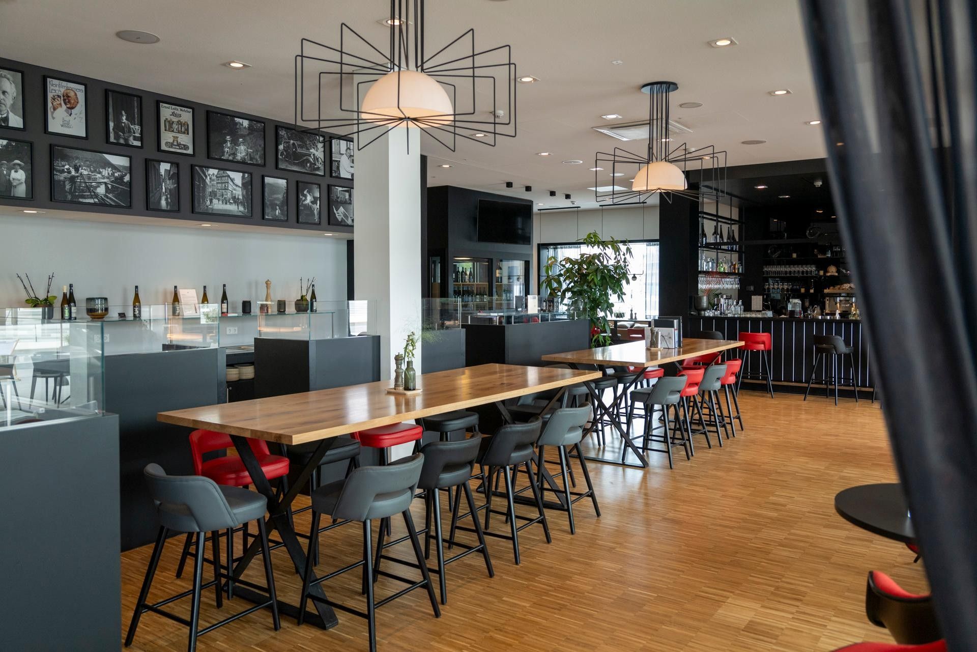 A modern bar area with a long wooden table, multiple bar stools, and a wall of framed photographs.