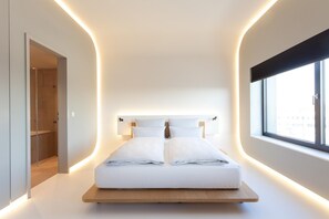 A modern bedroom with a bed centered on a platform, a large window on one side, and a shower area on the other. - Ernst Leitz Hotel Wetzlar (Wetzlar)