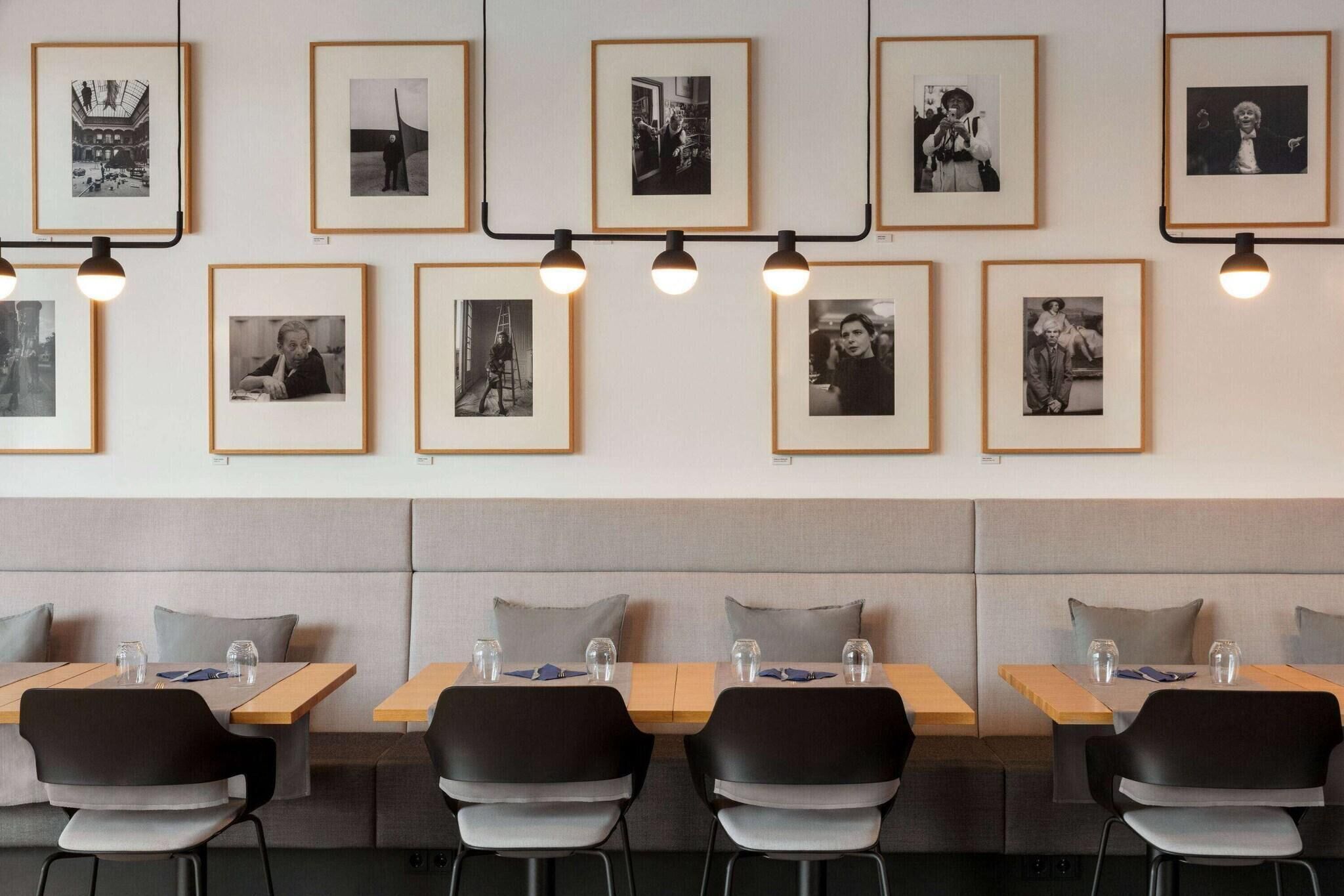 A restaurant with framed black and white photos on the wall, cushioned seating, and tables with glasses and napkins.