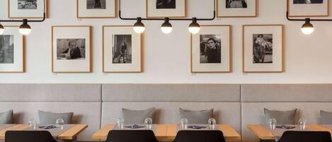 Un restaurant dont les murs sont ornés de photographies en noir et blanc encadrées, avec des sièges confortables et des tables où l’on trouve des verres et des serviettes.