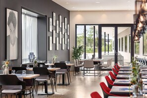 A modern restaurant with a long dining area, black and red chairs, and a large window providing a view of the outdoors. - Ernst Leitz Hotel Wetzlar (Wetzlar)