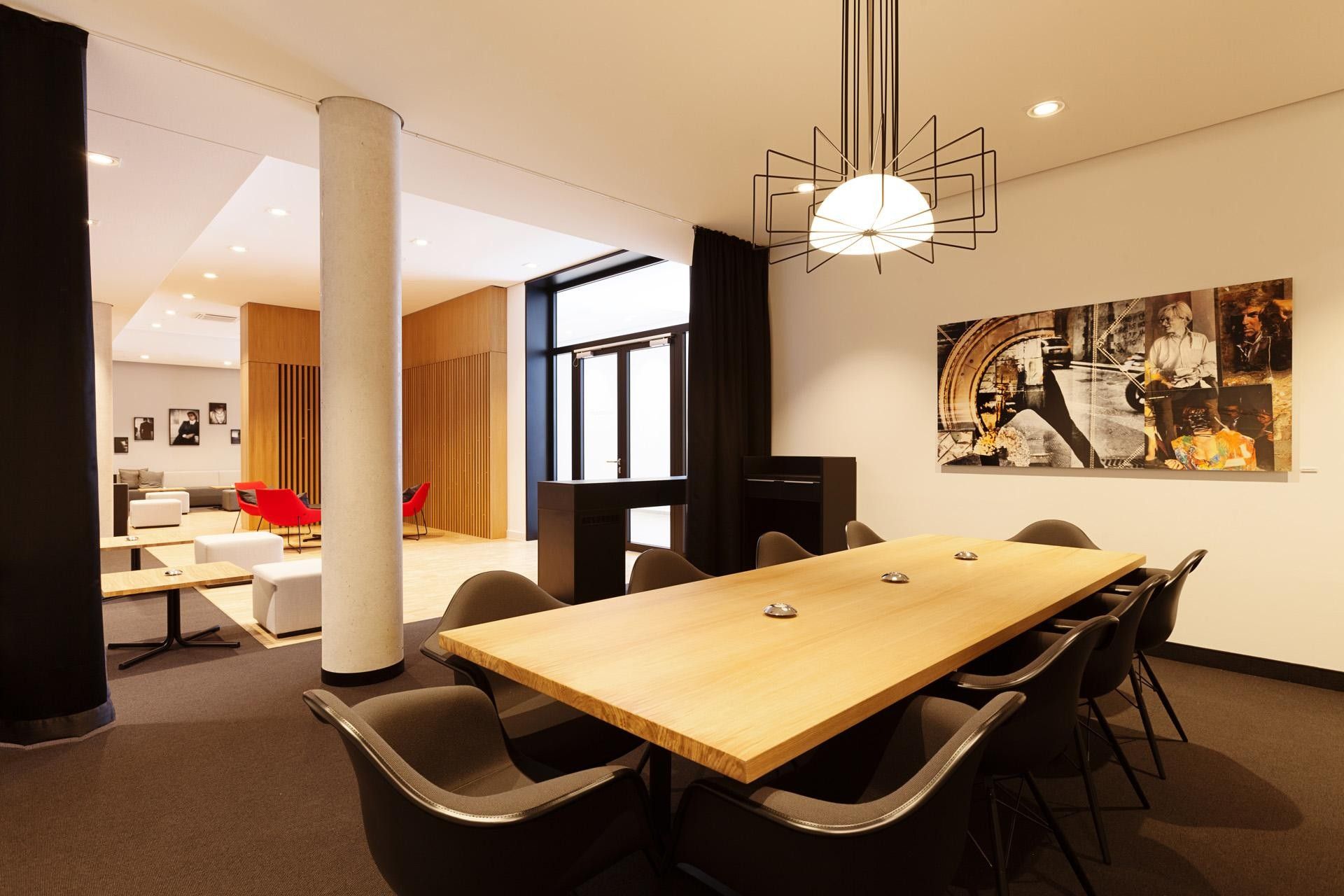 Une salle de conférence moderne, dotée d’une table en bois, de chaises noires et d’un luminaire suspendu au design géométrique original.