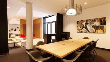Une salle de conférence moderne, dotée d’une table en bois, de chaises noires et d’un luminaire suspendu au design géométrique original.
