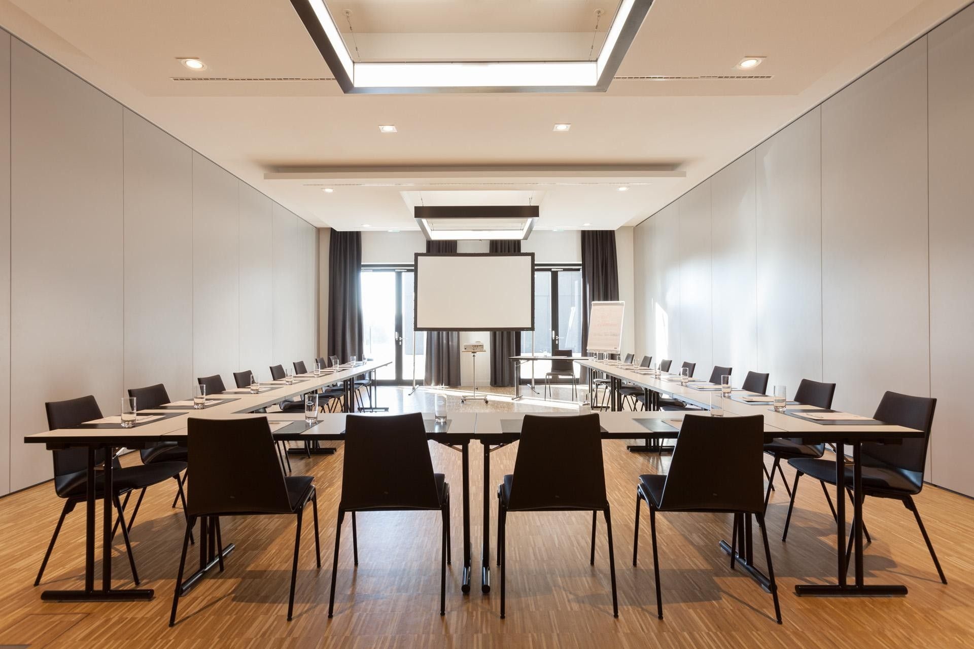 Ein Konferenzraum mit langen Tischen, Stühlen, einer großen Leinwand und einem Projektor.