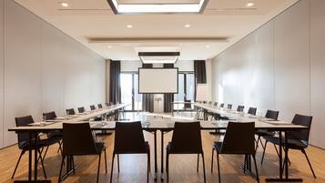 Ein Konferenzraum mit langen Tischen, Stühlen, einer großen Leinwand und einem Projektor.