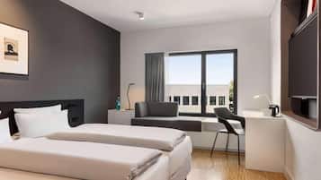 Habitación de hotel moderna con cama, escritorio, silla y un ventanal grande.