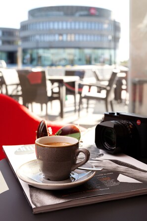 A cup of coffee on a saucer with a camera and a menu on a table. - Ernst Leitz Hotel Wetzlar (Wetzlar)