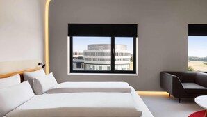 A modern hotel room with a bed, a sofa, a window with a view of a building, and a small table. - Ernst Leitz Hotel Wetzlar (Wetzlar)
