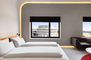 A modern hotel room with a bed, a sofa, a window with a view of a building, and a small table. - Ernst Leitz Hotel Wetzlar (Wetzlar)