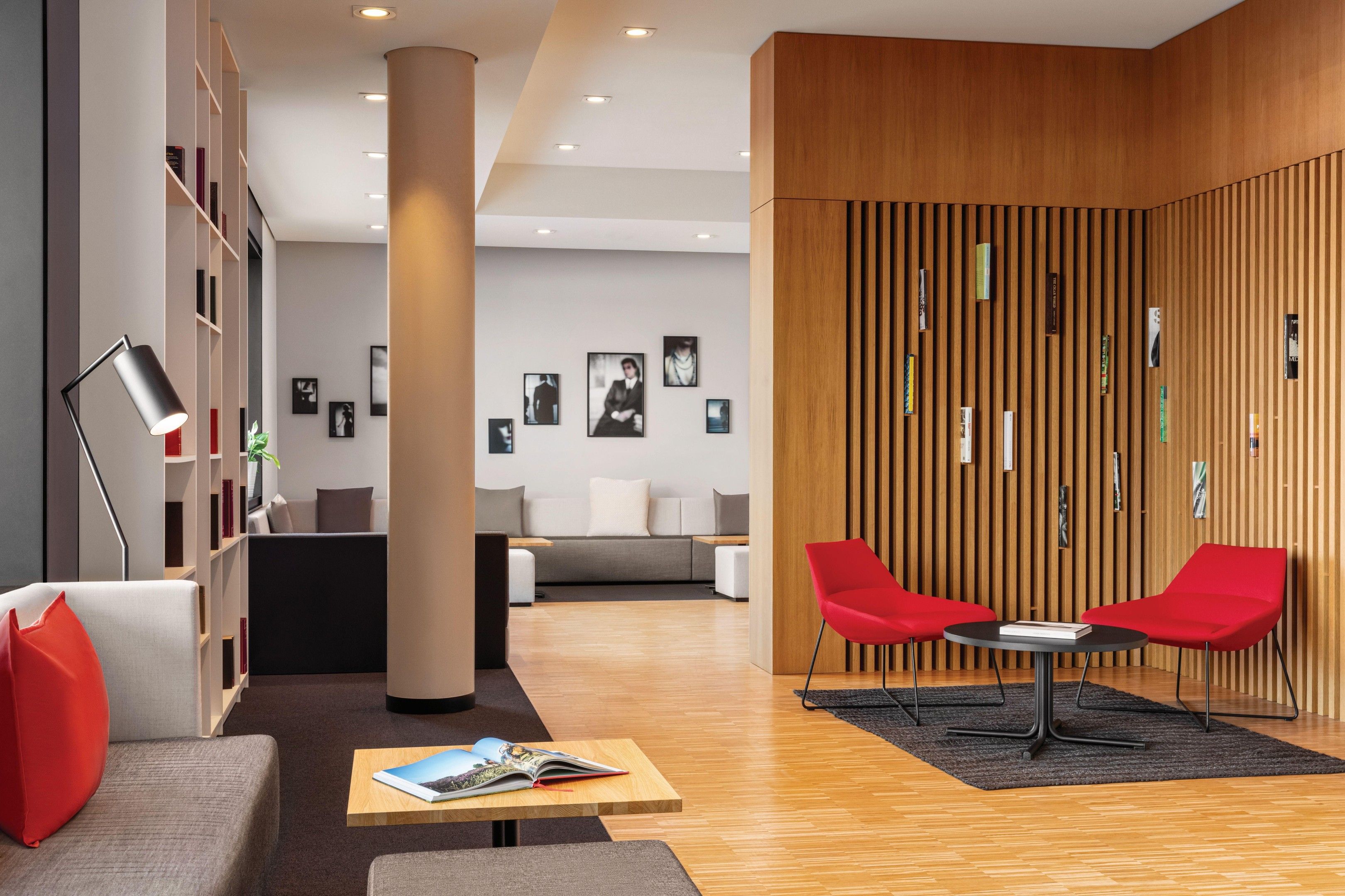 Un hall d’entrée moderne avec un mur en bois, des fauteuils rouges, un canapé et une bibliothèque.