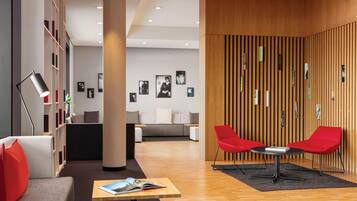 A modern lobby with a wooden wall, red chairs, a sofa, and a bookshelf.