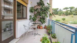 Uma varanda com mesa, cadeiras, plantas em vasos e vista para o jardim.
