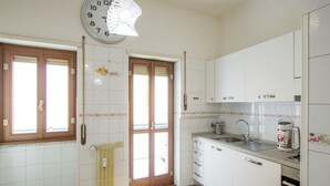 Cozinha com armários brancos, pia, fogão e um relógio na parede.
