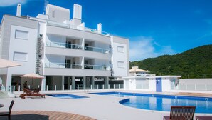 A modern hotel with a pool area, outdoor seating, and a view of a green hill. - Praia dos Ingleses Belo Recanto da Ilha (Florianópolis)