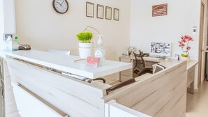 A modern reception desk with a clock, framed certificates, and a potted plant. - Nova Hotel (Cadereyta Jimenez)