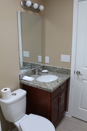 A bathroom with a white toilet, a sink, and a mirror above it. There are three light fixtures above the mirror. - Quiet Clean and Comfortable Room (Seattle)