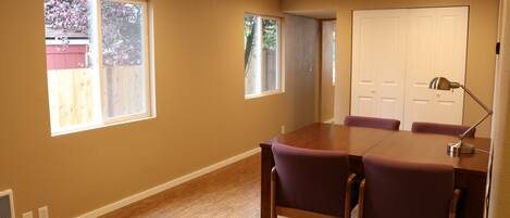 A dining area with a wooden table and purple chairs, large windows, and a white door.