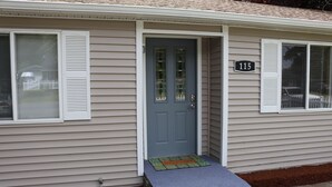 A single-story house with a blue front door, a number '115' sign, and a small porch with a welcome mat.