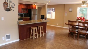A modern kitchen with a central island, wooden bar stools, and a dining area with a wooden table and chairs.