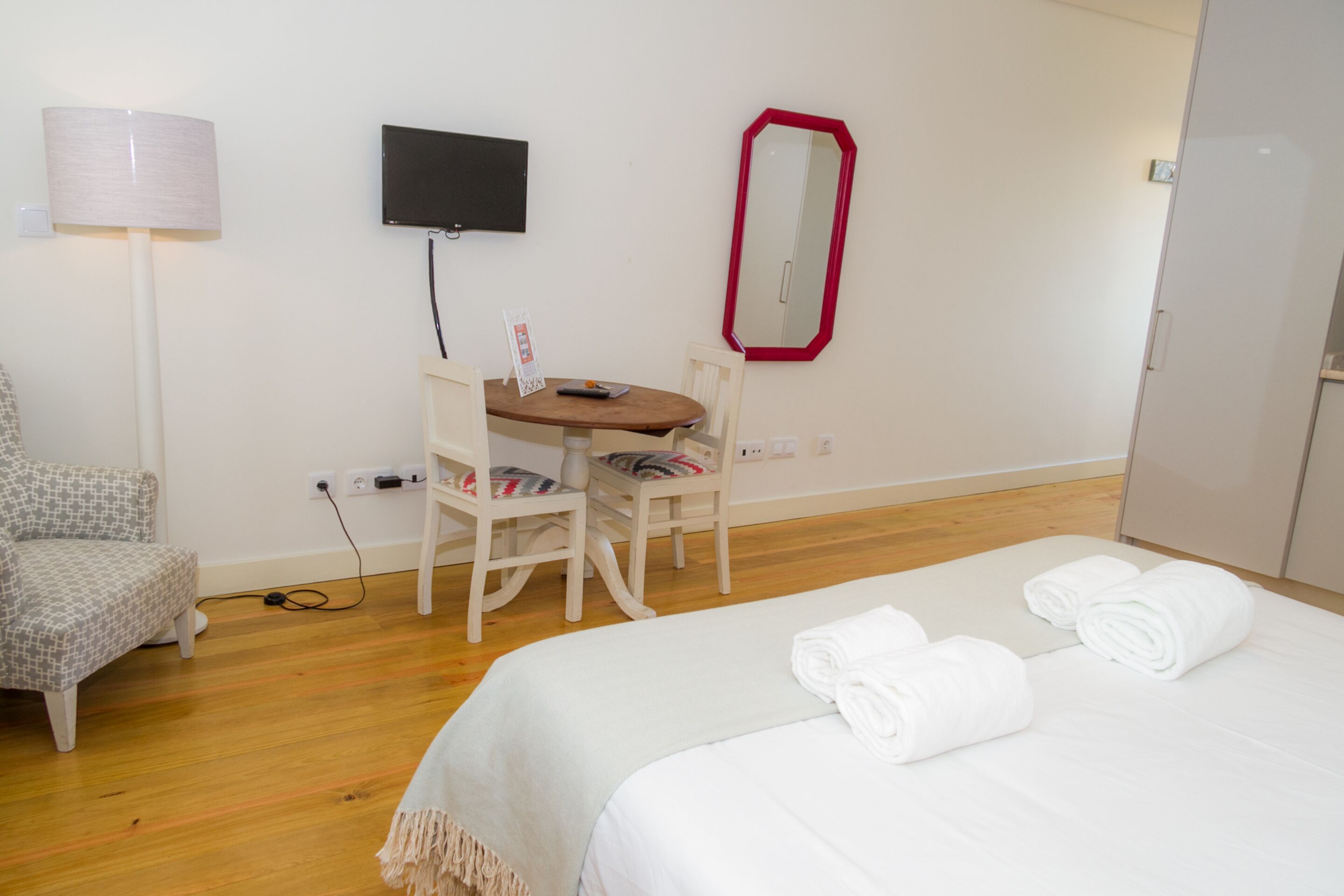 A hotel room with a bed, a desk, a chair, a TV, and a mirror.