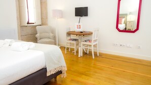A hotel room with a bed, a round table with chairs, a television, a mirror, and a window with curtains. - Liiiving in Porto - Historic Clerigos Studio 4F (Porto)