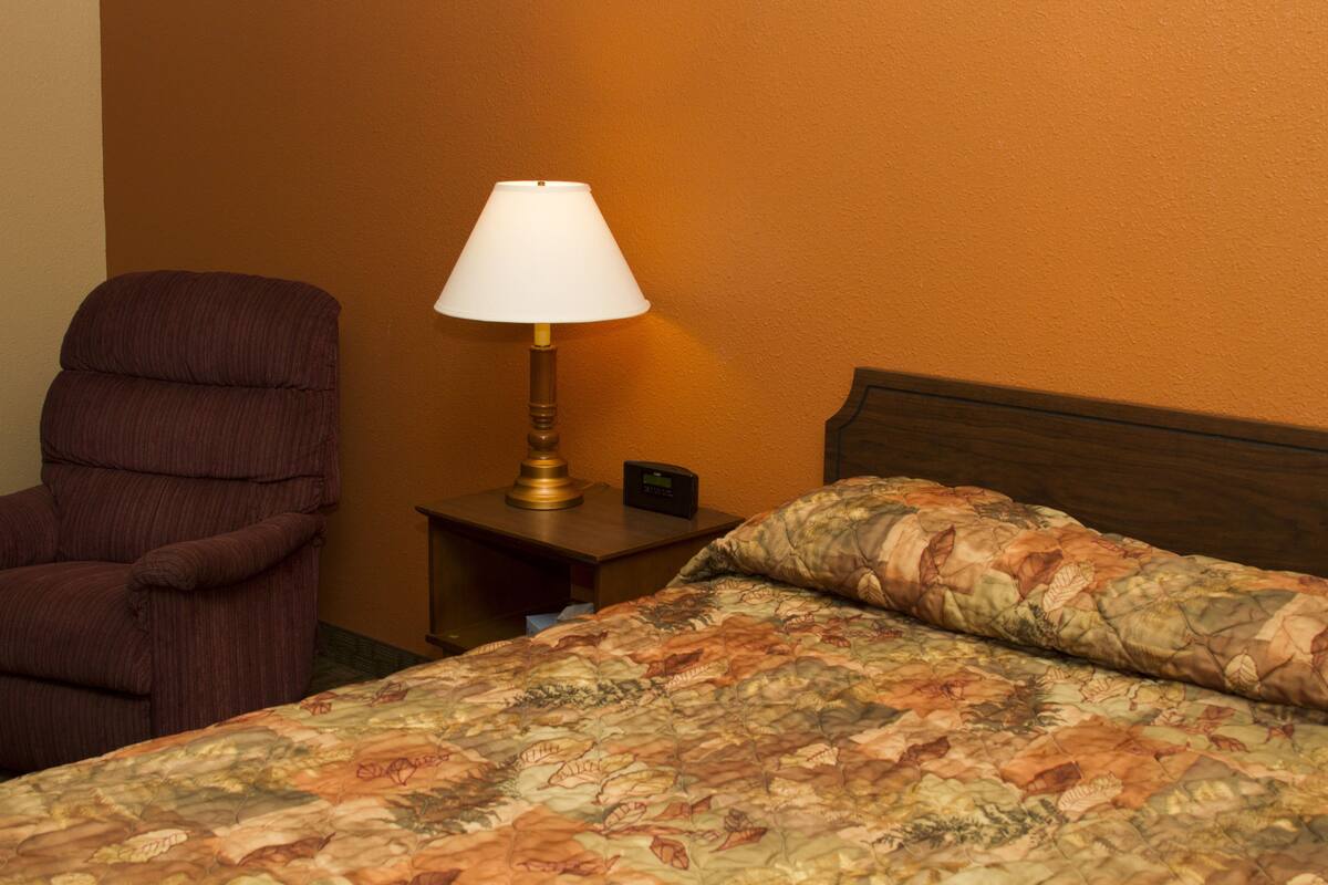 A hotel room with a bed, a chair, a nightstand, and a lamp.