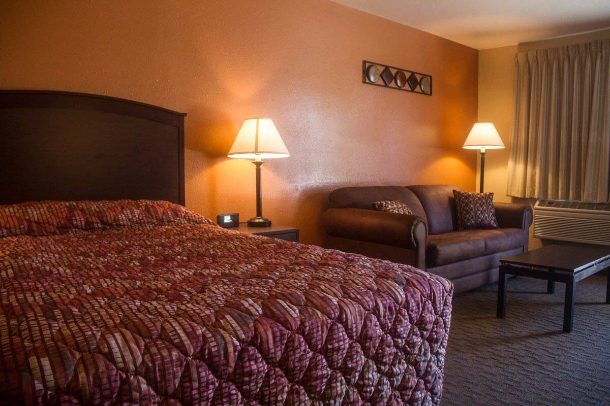 A hotel room with a large bed, a sofa, two bedside lamps, a small table, and a window with curtains.