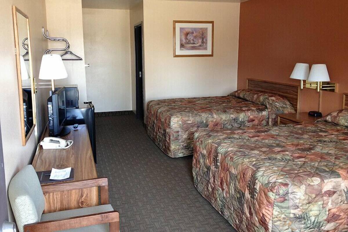 A hotel room with a desk, two beds, a television, and a framed picture on the wall.