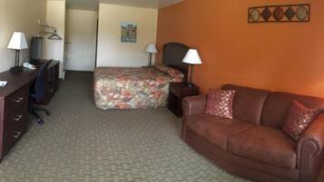 A hotel room with a bed, a sofa, a desk with a computer, and a lamp.