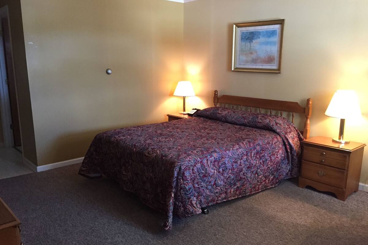 A neatly made bed with a patterned bedspread, two bedside tables with lamps, and a framed picture on the wall.