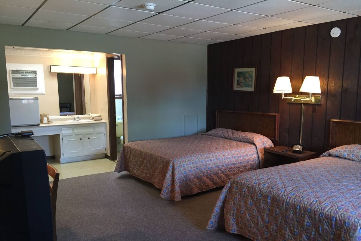 A hotel room with two beds, a desk, a dresser, a mirror, and a bathroom visible through an open door.