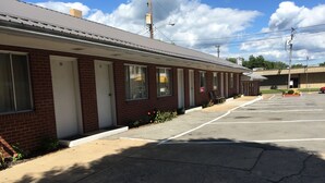 Um motel com quartos numerados, um estacionamento e céu claro.