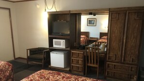 Quarto de hotel com duas camas, uma escrivaninha com micro-ondas, frigorífico, uma cadeira e um guarda-roupa.