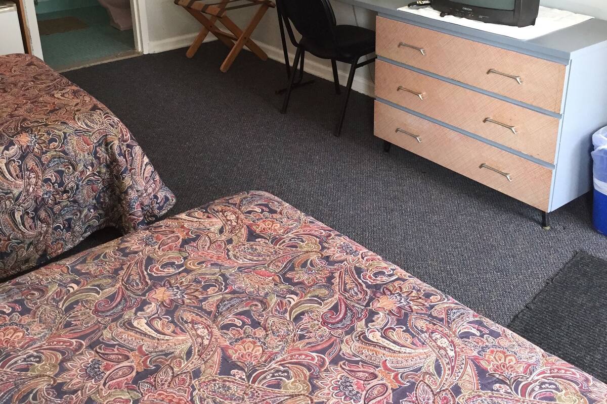 A bedroom with a bed, a desk, a chair, a television, and a dresser.