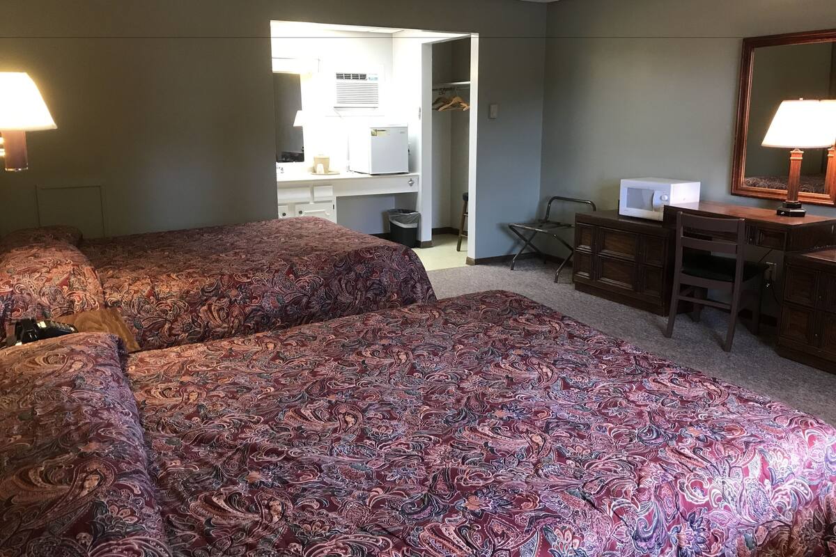 A hotel room with two beds, a desk, a chair, a dresser, and a mirror.